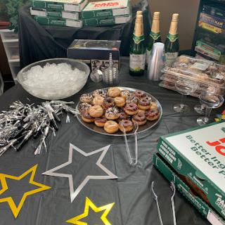 A festive party spread featuring donuts, pizza boxes, and sparkling beverages.
