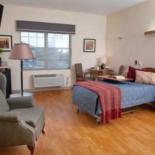 A cozy bedroom featuring a bed, armchair, and window with natural light.