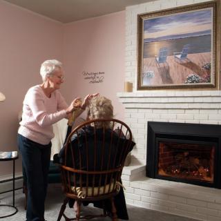 An elderly woman styles another's hair in a cozy living room setting.