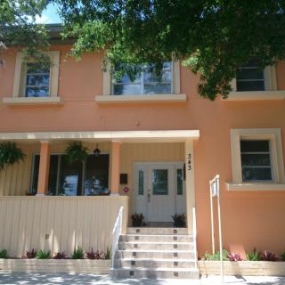 A two-story peach-colored house with a front porch and surrounding greenery.