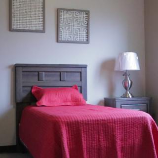 A minimalist bedroom featuring a single bed with vibrant red bedding and a modern nightstand topped with a stylish lamp.