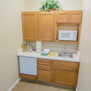 A compact kitchenette with wooden cabinets, a sink, and a microwave.