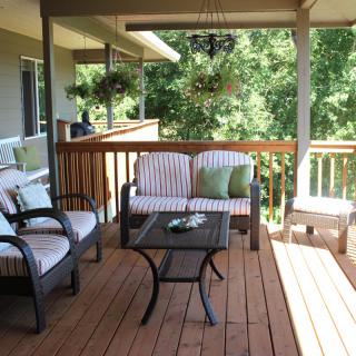 A cozy outdoor patio with seating and a glass-top table, surrounded by nature.