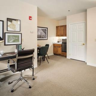 A modern office space with a desk, chair, and artwork, adjacent to a kitchenette.