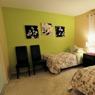 A cozy bedroom with twin beds, featuring a green accent wall and floral artwork.
