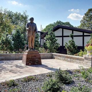 A statue in a garden setting with modern architecture in the background.