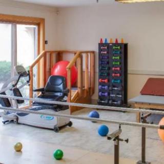 A therapy room equipped with exercise machines, fitness balls, and parallel bars for rehabilitation.