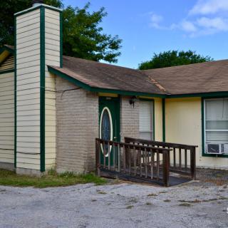 A small house with a chimney and porch, featuring a front door with an oval window.