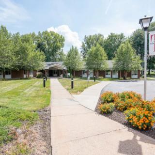 A pathway leads to a building surrounded by trees and flowers on a sunny day.