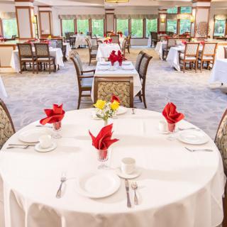 A beautifully set restaurant dining room with elegant white tablecloths and red napkin accents.