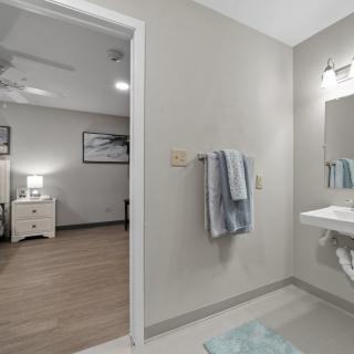 A modern bathroom with a view into a neatly decorated bedroom, showcasing neutral tones and contemporary design.