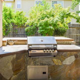 An outdoor built-in grill setup in a sunny backyard patio.
