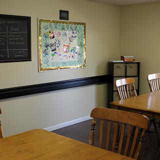 A cozy dining area with wooden tables and chairs, featuring a bulletin board and chalkboard on the walls.