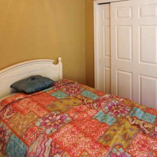 A cozy bedroom with a colorful quilt and a small pillow on the bed, set against a neutral wall with a white wardrobe.