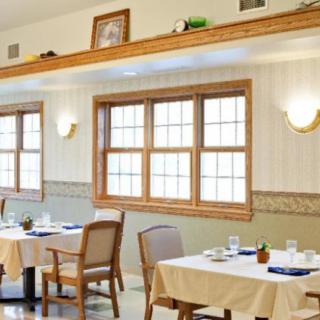 A cozy dining room with neatly arranged tables and chairs, featuring large windows and warm lighting.