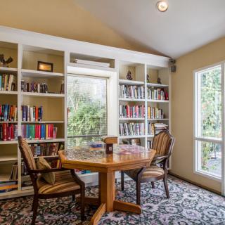 A cozy reading room with bookshelves, a round table, and chairs by the window.
