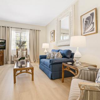 A cozy living room with a blue sofa, wooden coffee table, and elegant decor, featuring artwork on the walls and a TV in the corner.
