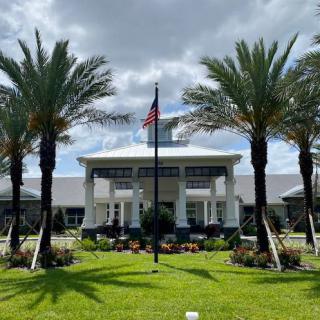 A symmetrical view of a building with palm trees and an American flag in front, set against a cloudy sky.