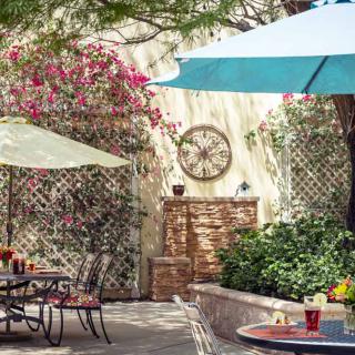 A charming outdoor patio area with tables and umbrellas, surrounded by lush plants and colorful flowers.
