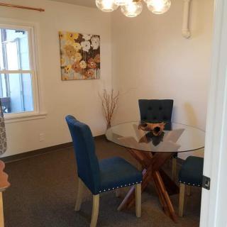 A modern dining room with a glass table and blue upholstered chairs, featuring wall art and a window.