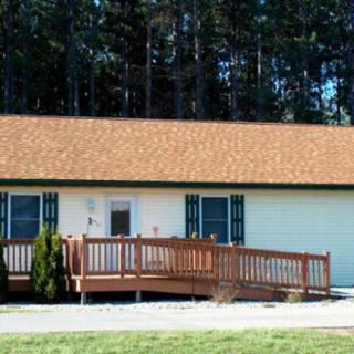 A single-story house with a wooden ramp and deck in front, surrounded by trees.