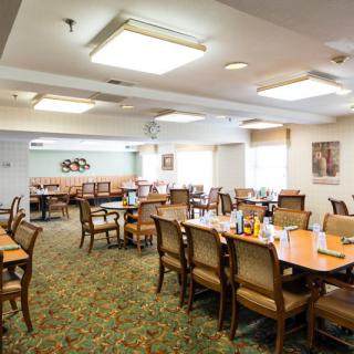 A well-lit dining room with several tables and chairs, featuring a carpeted floor.