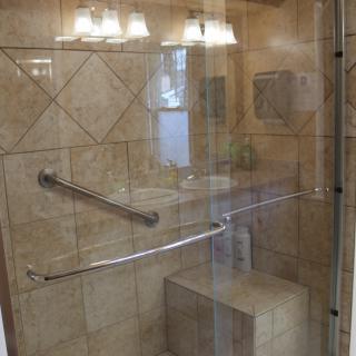 Modern shower with glass door, tiled walls, seating, and grab bars.