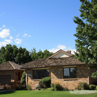 A suburban brick house with a green lawn and surrounded by trees under a clear blue sky.