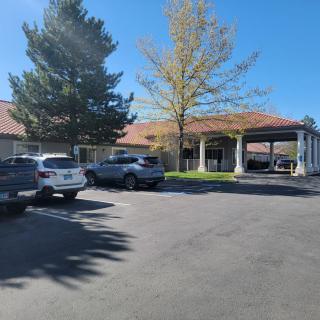 A sunny day view of a building with a parking lot and several cars in front.