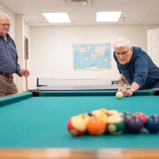 Two people engaged in a game of billiards in a recreation room.