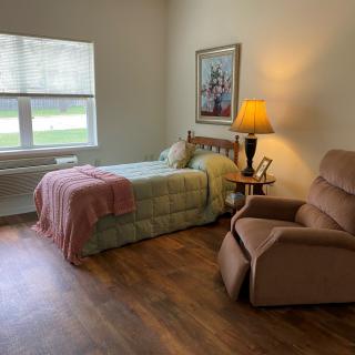 A cozy bedroom with a single bed, recliner chair, and natural light from the window.