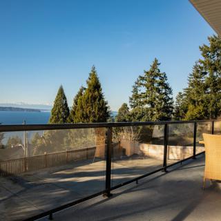 A scenic view from a balcony overlooking trees and a distant coastline under a clear blue sky.