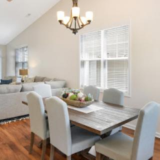 A stylish dining area featuring a wooden table surrounded by gray upholstered chairs, illuminated by a modern chandelier.