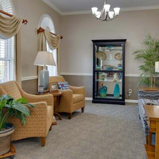 A cozy living room with wicker chairs, decorative plants, and a glass cabinet.
