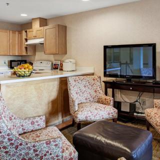 A cozy living room with a kitchenette, featuring floral armchairs and a flat-screen TV.