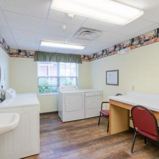 A well-lit laundry room with two washing machines, a dryer, a folding table, and a chair.