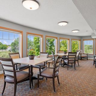 A bright dining area with multiple tables and chairs, surrounded by large windows letting in natural light.