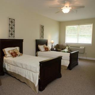 A cozy bedroom with two twin beds, neatly arranged furniture, and ample natural light streaming through the window.