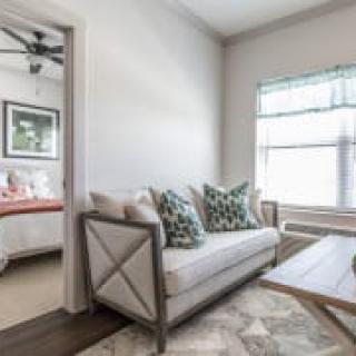 A cozy living room with a sofa, decorative pillows, and a view into the adjacent bedroom.