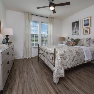 A modern bedroom with stylish decor, featuring a bed, artwork on the walls, and large windows letting in natural light.