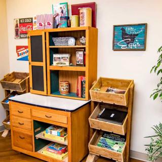 A children's play kitchen set with wooden shelves, baskets, and a miniature chalkboard.