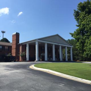 A brick building with large white columns and a driveway under a clear blue sky.