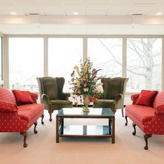 A well-lit living room with elegant furniture, including red sofas, green armchairs, and a central coffee table.
