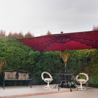 A cozy outdoor patio setup with a red umbrella, a table with chairs, and a decorative bench surrounded by greenery.