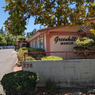 Exterior view of a building named Greenhill Manor with surrounding trees and landscaping.