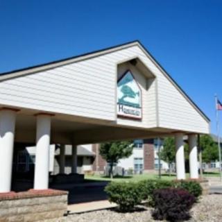 A building entrance with a gabled roof and columns, surrounded by shrubs.