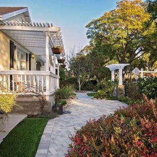 A beautifully landscaped garden with a walkway leading up to a charming house, surrounded by trees and shrubs.
