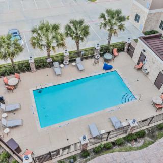 An aerial view of an outdoor swimming pool surrounded by lounge chairs and palm trees.