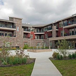 Modern residential building with landscaped surroundings and a central walkway under a cloudy sky.