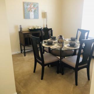 A cozy dining room with a round table set for four, featuring elegant decor and a sideboard with artwork above it.